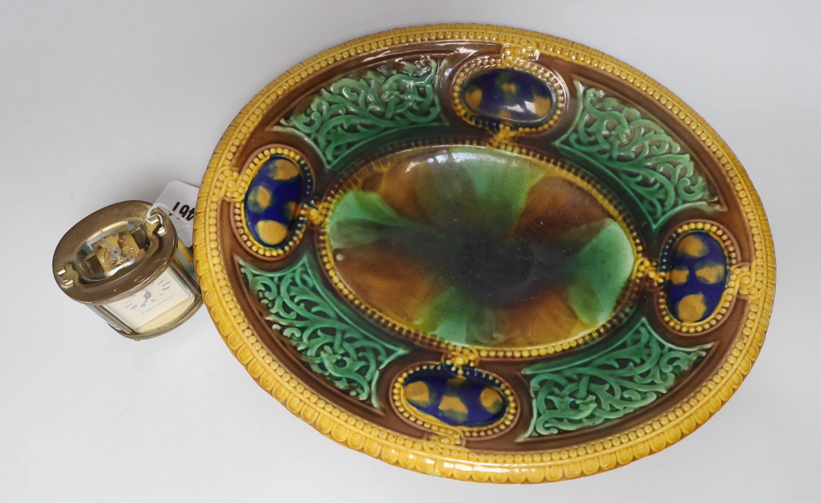 A small oval lacquered brass carriage timepiece retailed by Mappin and Webb together with an oval majolica dish. 32cm long